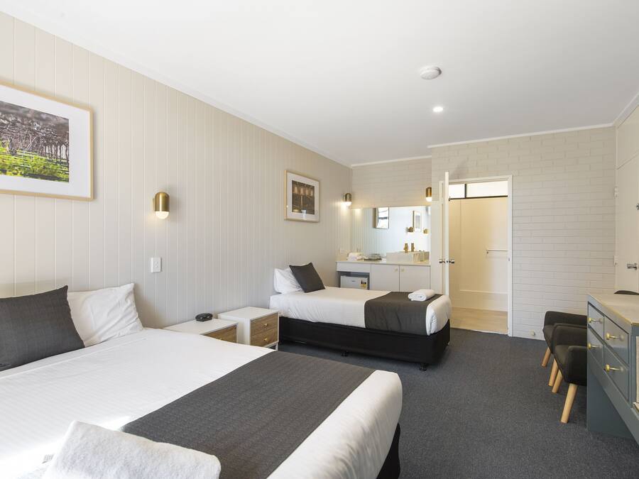 A hotel room with two beds, a desk, a chair, a mirror, and a bathroom visible through an open door.