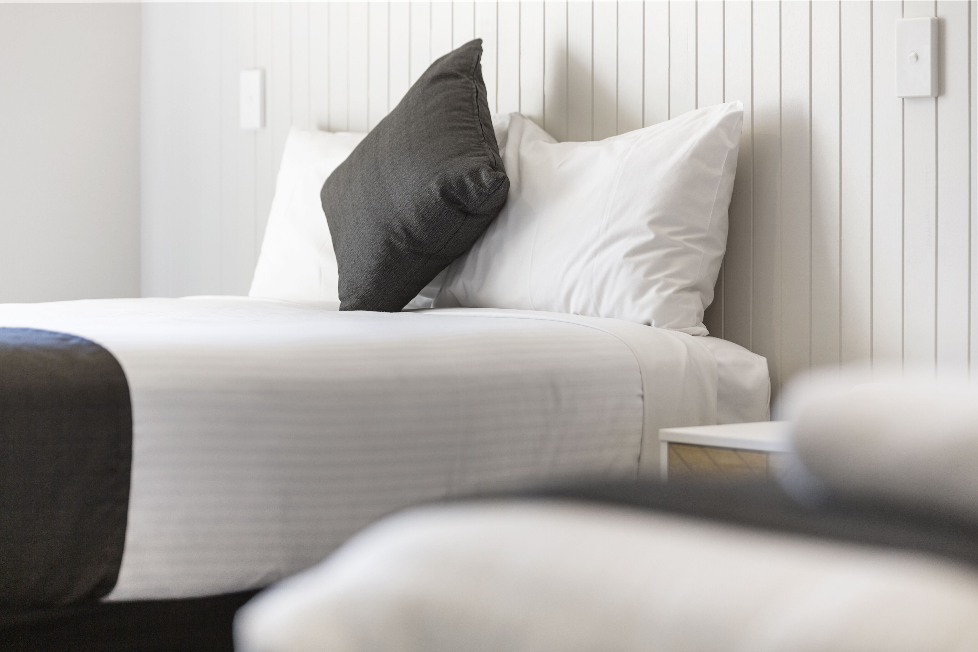 Una cama bien hecha con ropa de cama blanca y almohada oscura.