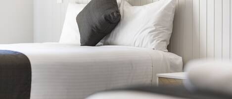 Una cama bien hecha con ropa de cama blanca y almohada oscura.