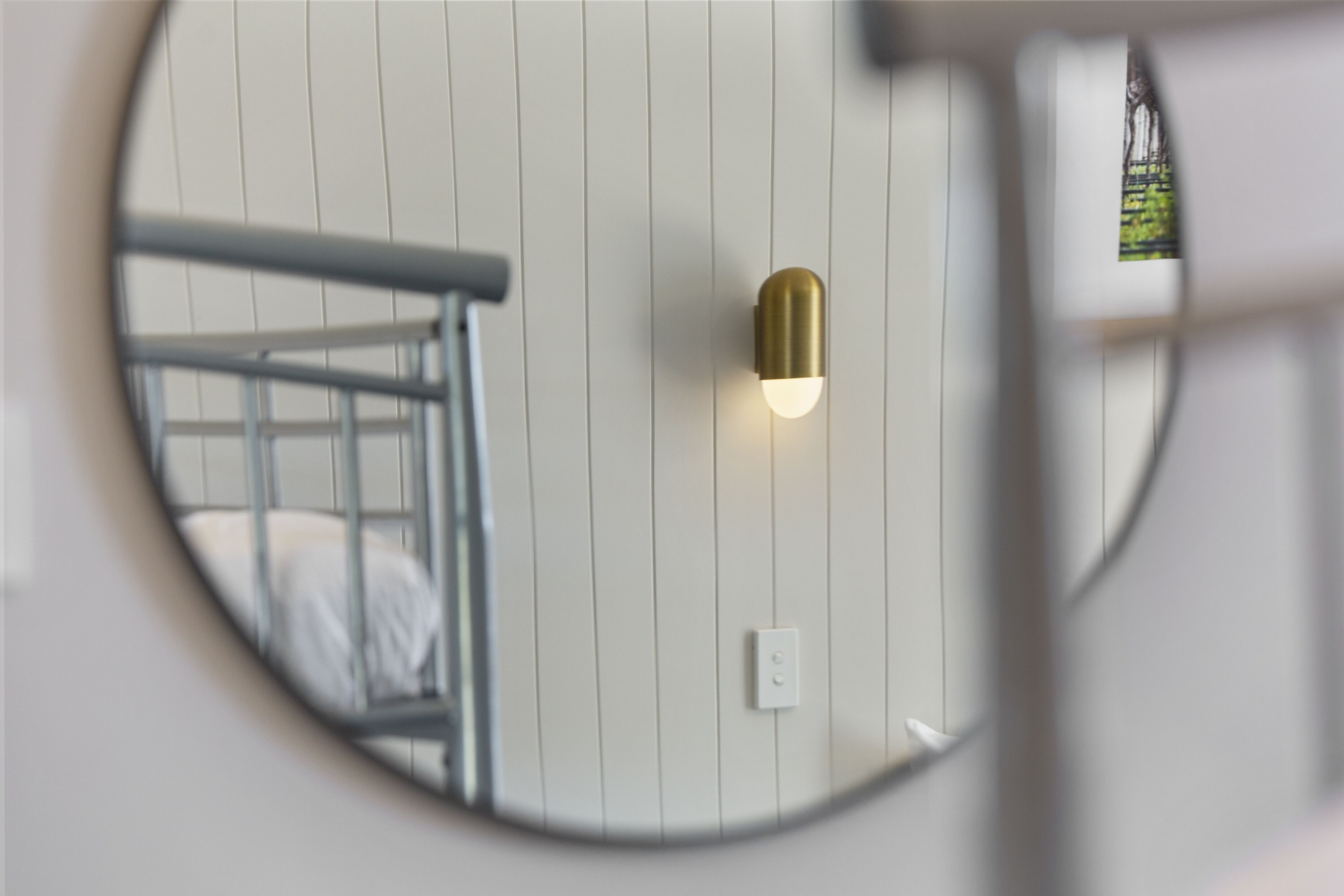 A circular mirror reflecting a bunk bed and a wall-mounted light fixture.