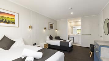 Habitación de hotel con dos camas, un escritorio, una silla, un espejo y baño visible a través de una puerta abierta.