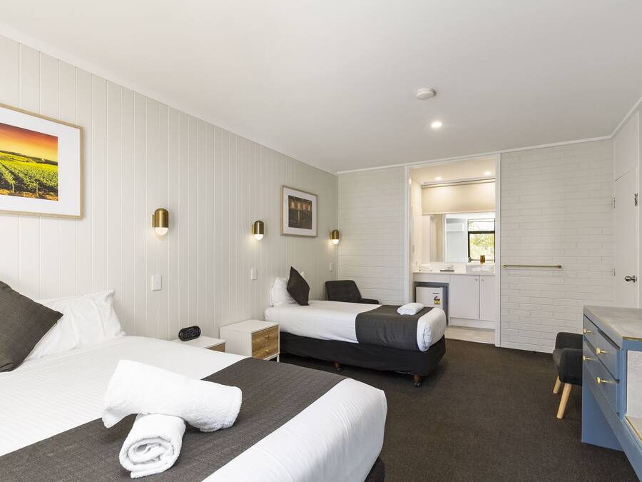 Habitación de hotel con dos camas, un escritorio, una silla, un espejo y baño visible a través de una puerta abierta.