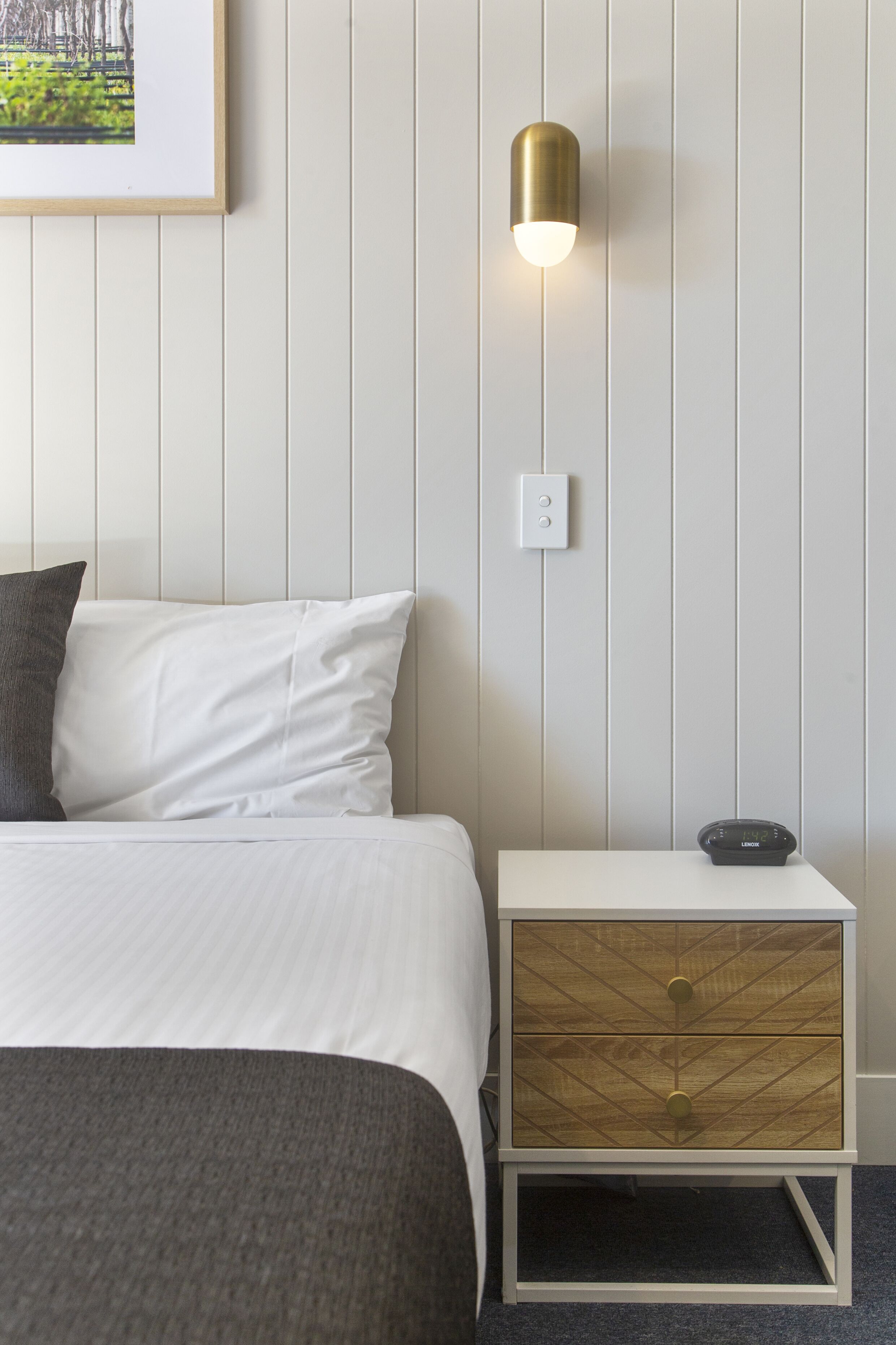 A neatly arranged bedroom with a bed, a bedside table with a lamp, and a wall-mounted light fixture.