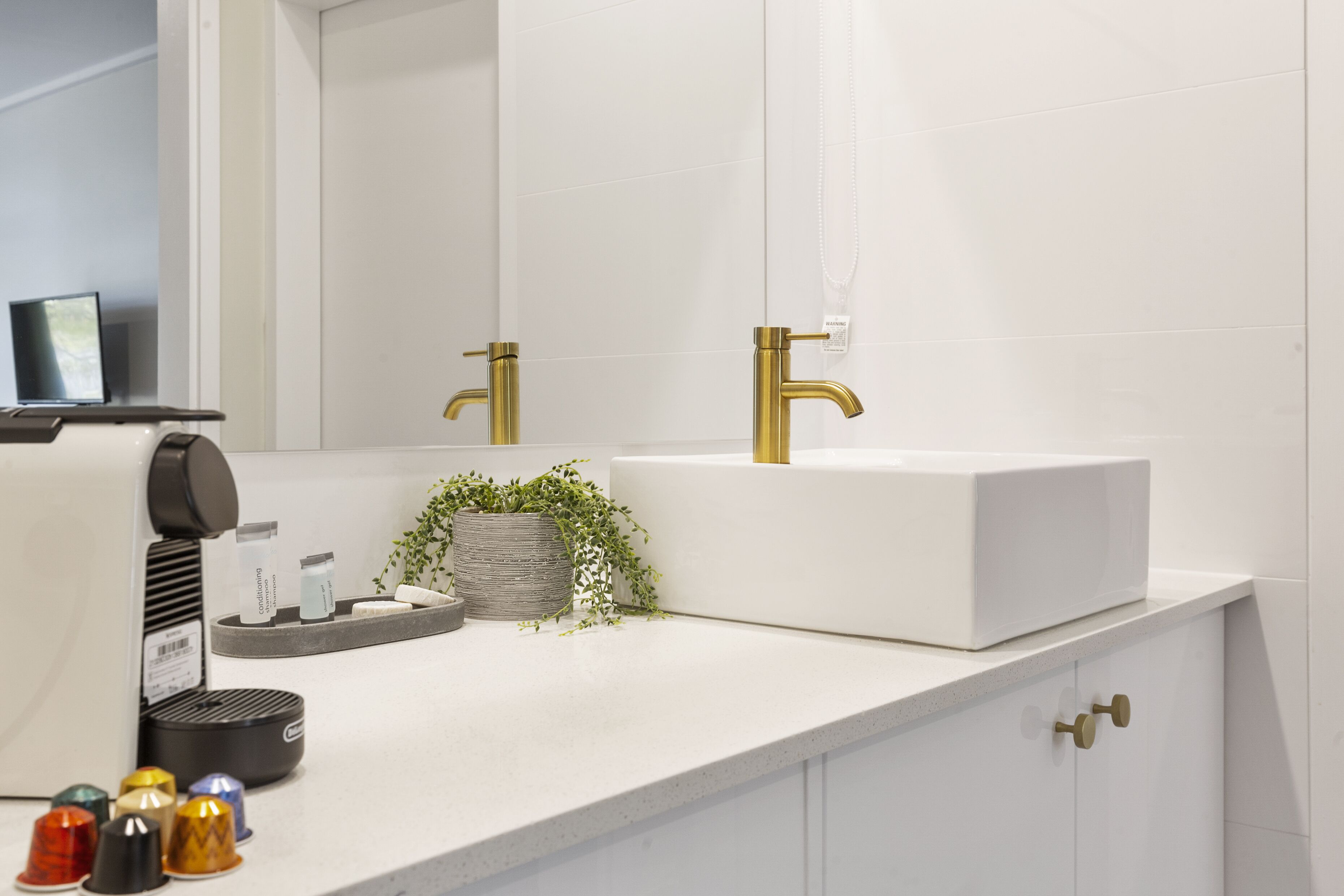 Un bagno moderno con un lavandino bianco, rubinetti dorati e uno specchio sopra.