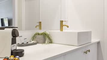 Un bagno moderno con un lavandino bianco, rubinetti dorati e uno specchio sopra.