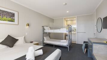 Habitación de hotel con literas, un escritorio, una silla, una mesita de noche y un cuadro en la pared.