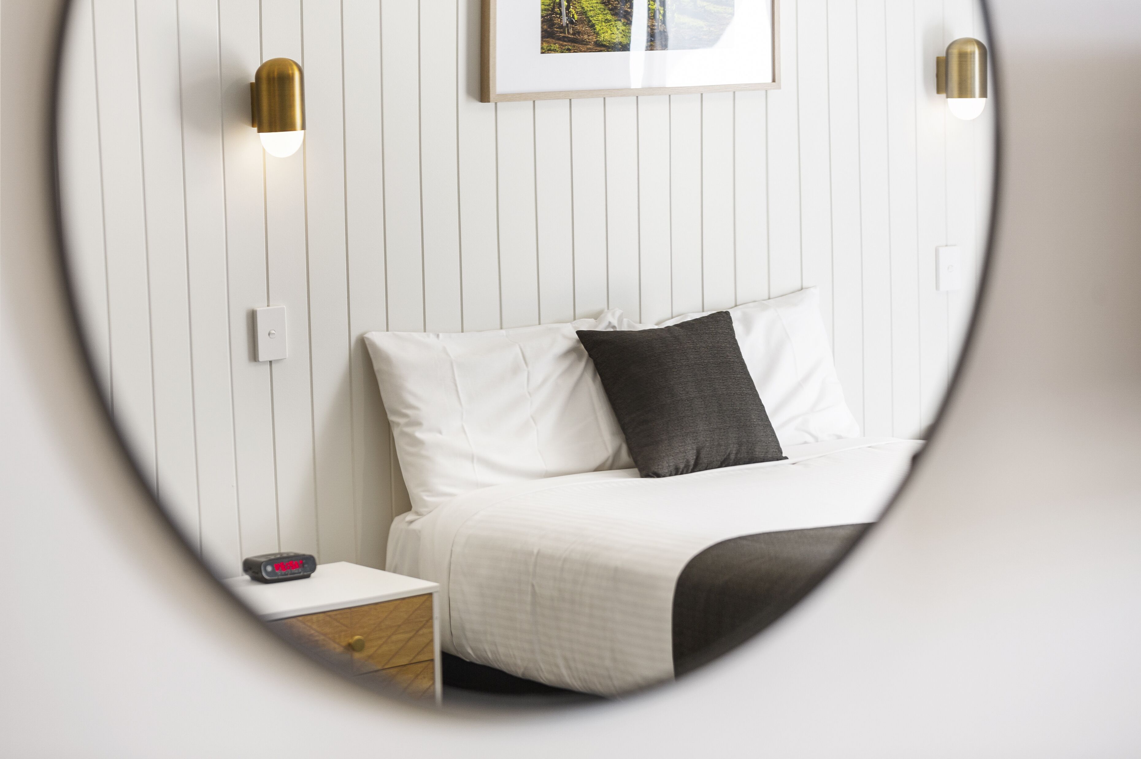 Een slaapkamer met een bed, nachtkastje, wandlamp en een lijst met een afbeelding aan de muur.
