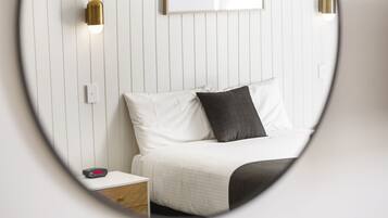 A bedroom with a bed, a nightstand, a wall-mounted light, and a framed picture on the wall.