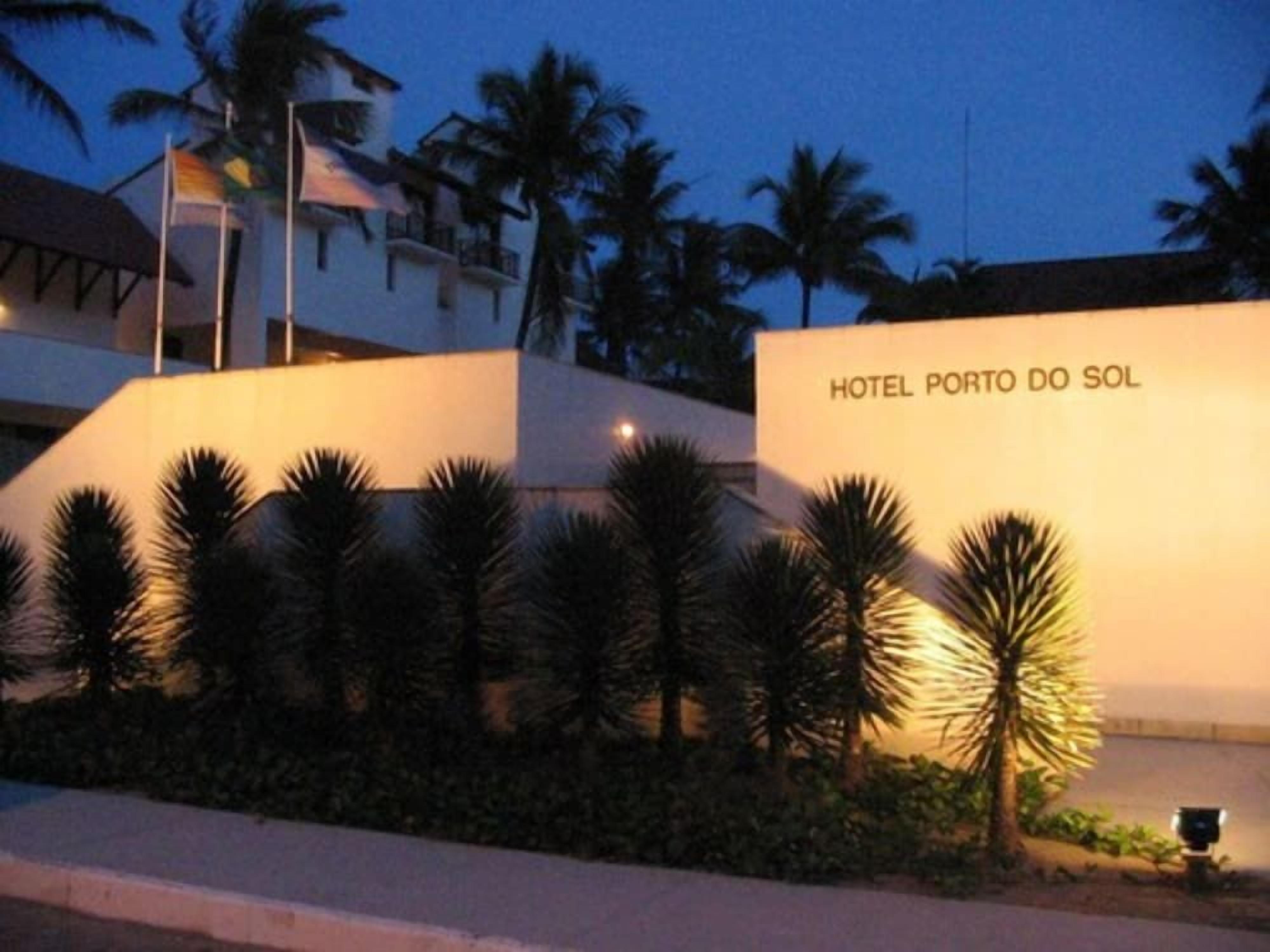 Um edifício com uma placa indicando 'HOTEL PORTO DO SOL' e palmeiras em frente.