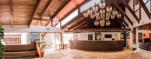 A reception area with a curved counter, wooden beams, and a hanging light fixture. - Porto Do Sol Hotel (GUARAPARI)