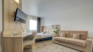A modern hotel room with a wooden desk, a bed, a sofa, and a TV mounted on the wall. - Eurotel (Perols)