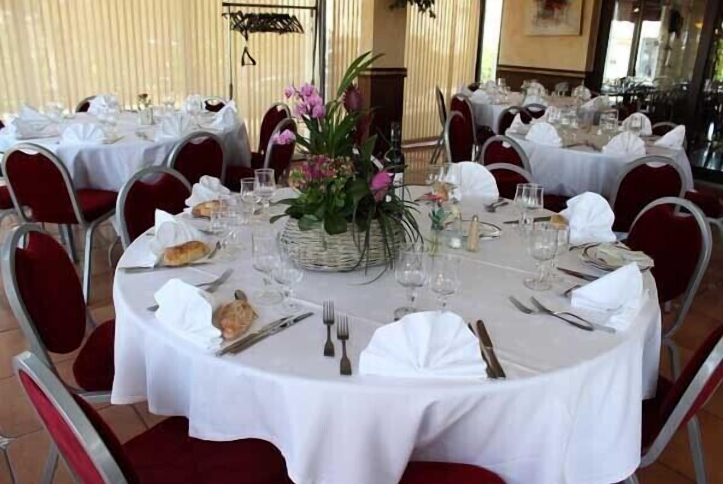 A restaurant with round tables set with white tablecloths, red chairs, and floral centerpieces.
