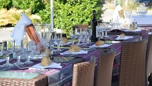 A dining table set outdoors with wicker chairs, wine glasses, and a bottle of wine. - Eurotel (Perols)
