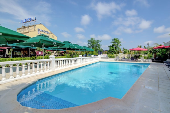 A swimming pool with a white balustrade, green umbrellas, and a Eurotel sign in the background.