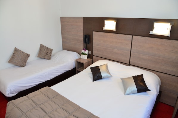 A hotel room with two single beds, each with a pillow and a bedside table. There is a telephone on the wall and a small nightstand with a vase of flowers.