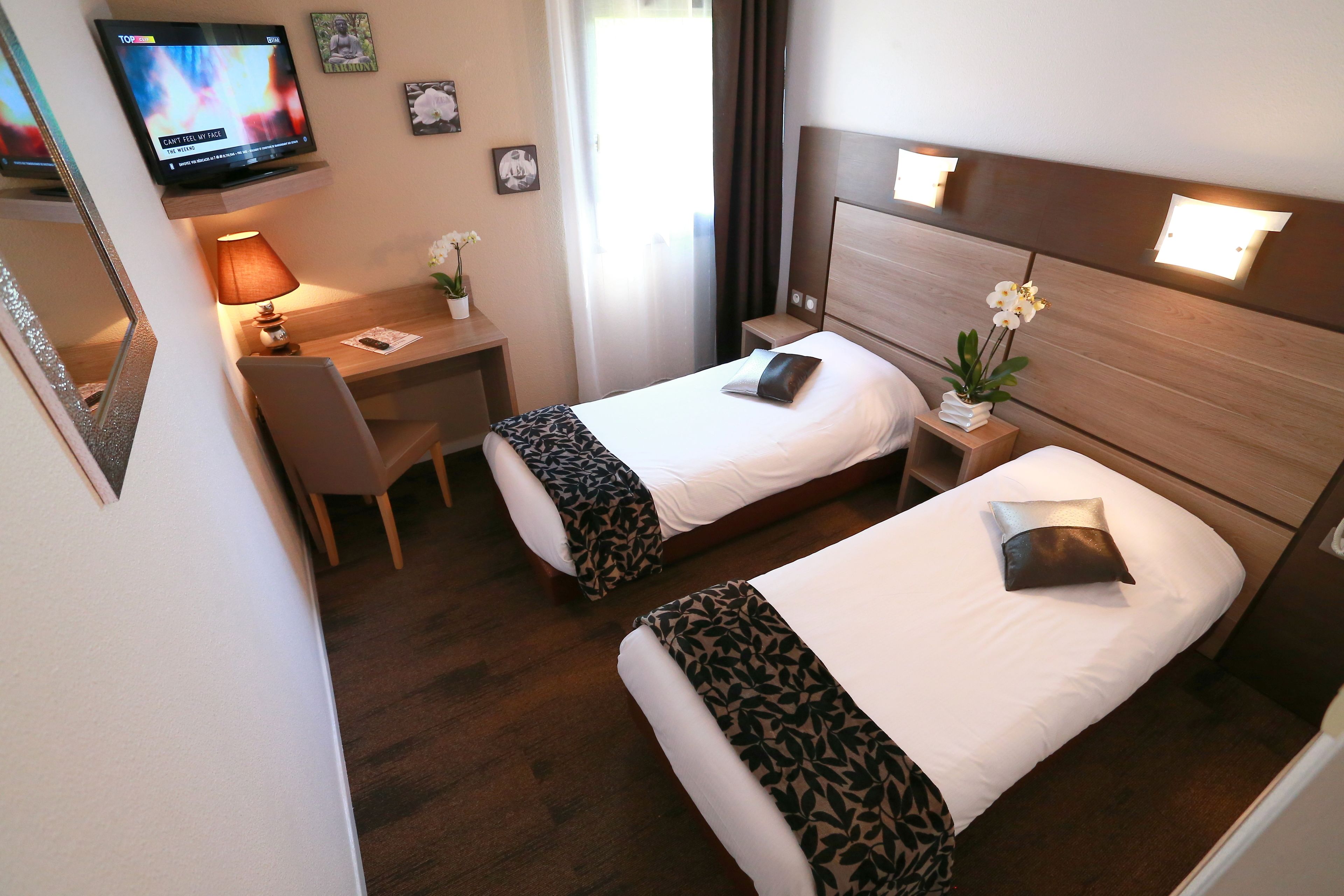 Une chambre d’hôtel avec deux lits, un bureau, une chaise, une télévision et une petite table avec une lampe et des fleurs.