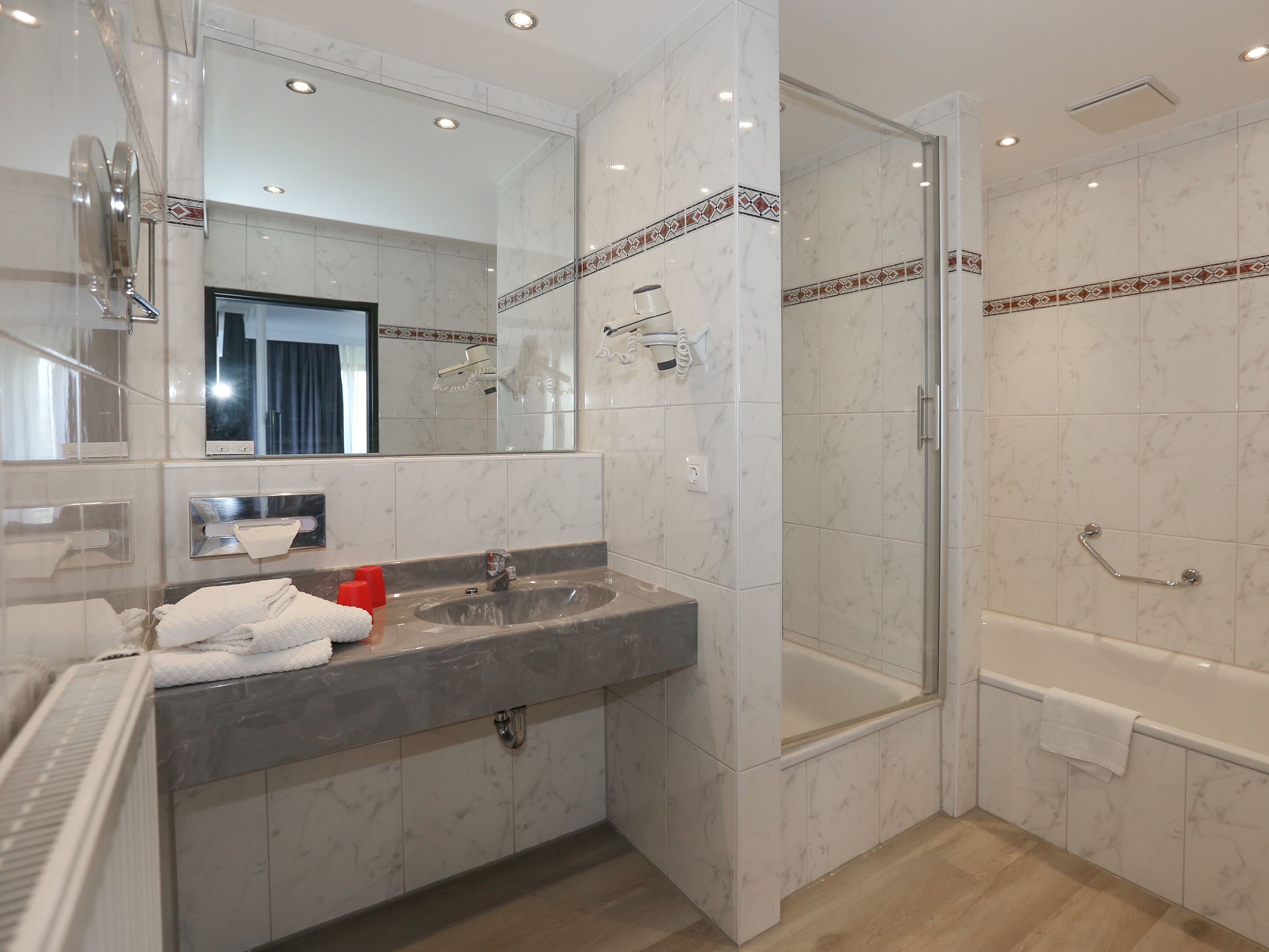Un baño moderno con lavamanos de mármol, ducha con mampara de vidrio y bañera.