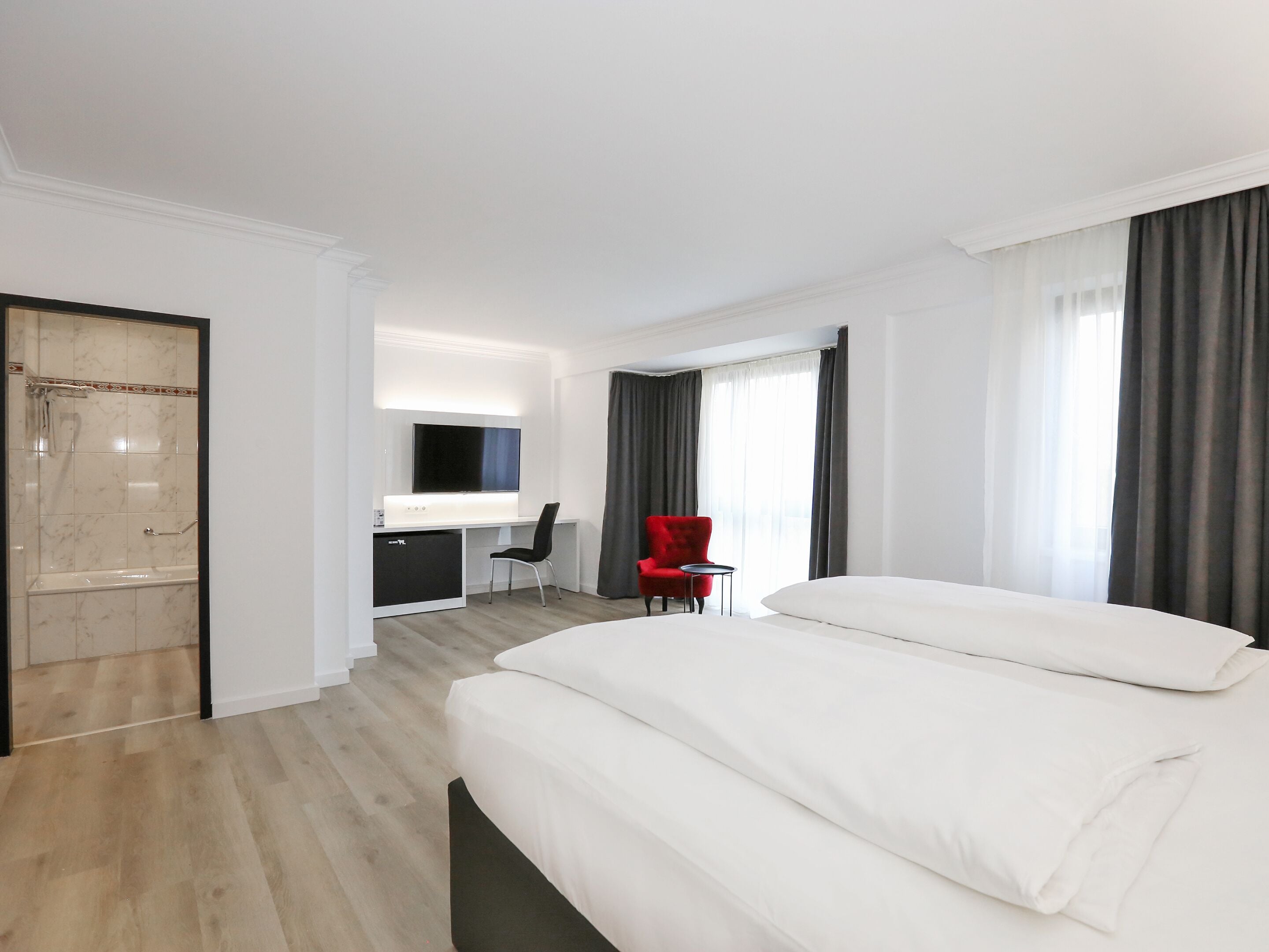 Een moderne hotelkamer met een groot bed, een bureau, een rode stoel en een douche.