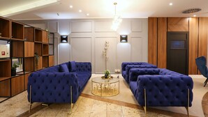 A modern living room with a blue sofa set, a round coffee table, and a bookshelf. - DORMERO Hotel Meerbusch (Meerbusch)