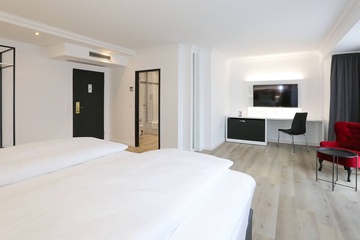 A hotel room with a bed, a desk, a chair, and a TV.