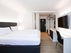 A modern hotel room with a large bed, a desk, and a TV.