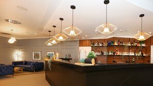 A modern bar area with a black counter, hanging pendant lights, and a wooden shelving unit displaying bottles and glasses. - DORMERO Hotel Meerbusch (Meerbusch)