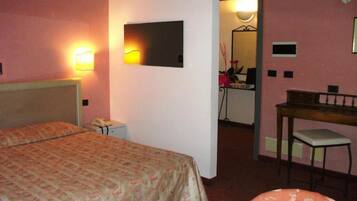 A hotel room with a bed, a desk, a chair, a mirror, and a small kitchenette.
