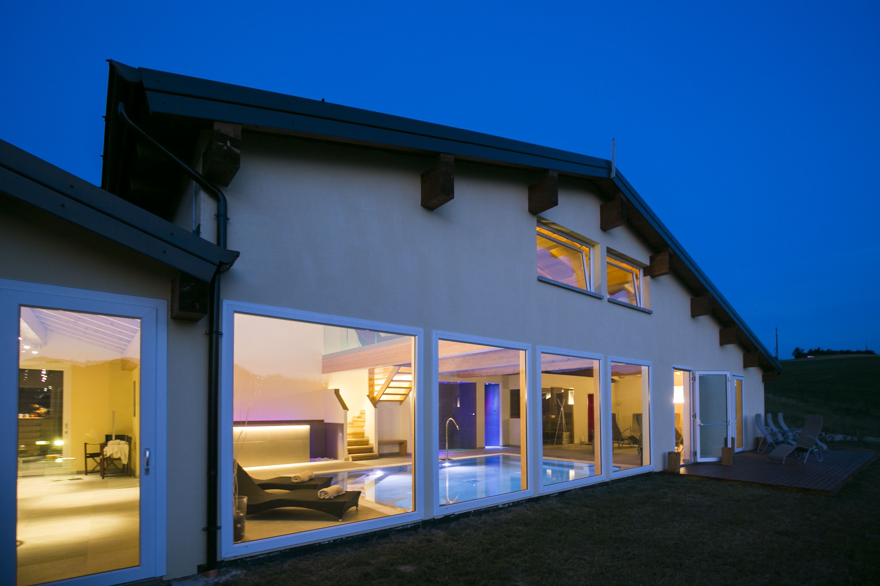 A modern house with large glass doors leading to a swimming pool area, a visible staircase, and outdoor seating.