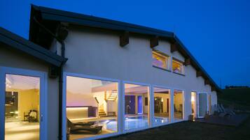 A modern house with large glass doors leading to a swimming pool area, a visible staircase, and outdoor seating.