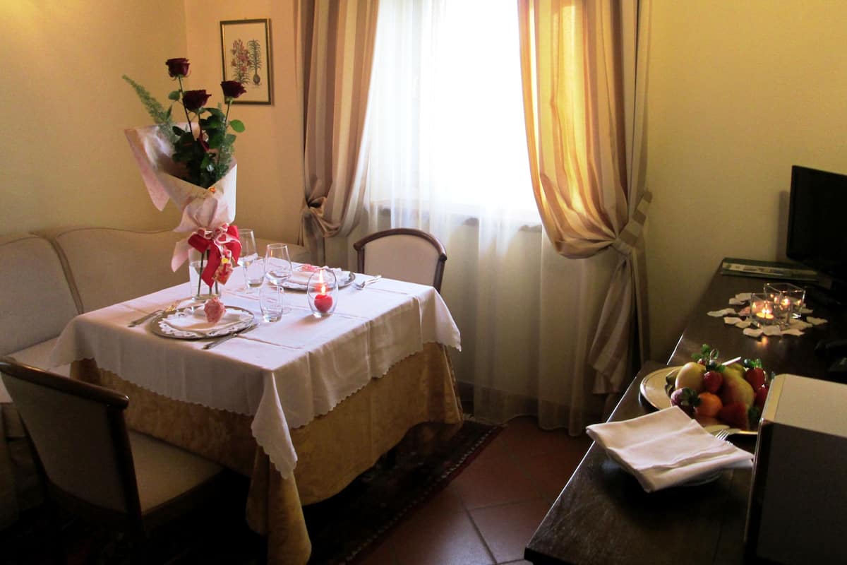 Un coin repas avec une table dressée pour deux personnes, une chaise, une petite table avec des fruits et un téléviseur posé sur un meuble.