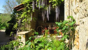 Un edificio rústico de piedra con un porche de madera cubierto de flores moradas colgantes.