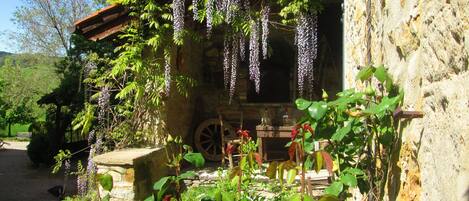 Un edificio rústico de piedra con un porche de madera cubierto de flores moradas colgantes.