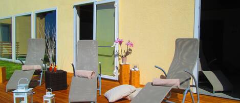 A deck with two lounge chairs, a small table with a vase of flowers, and two lanterns.