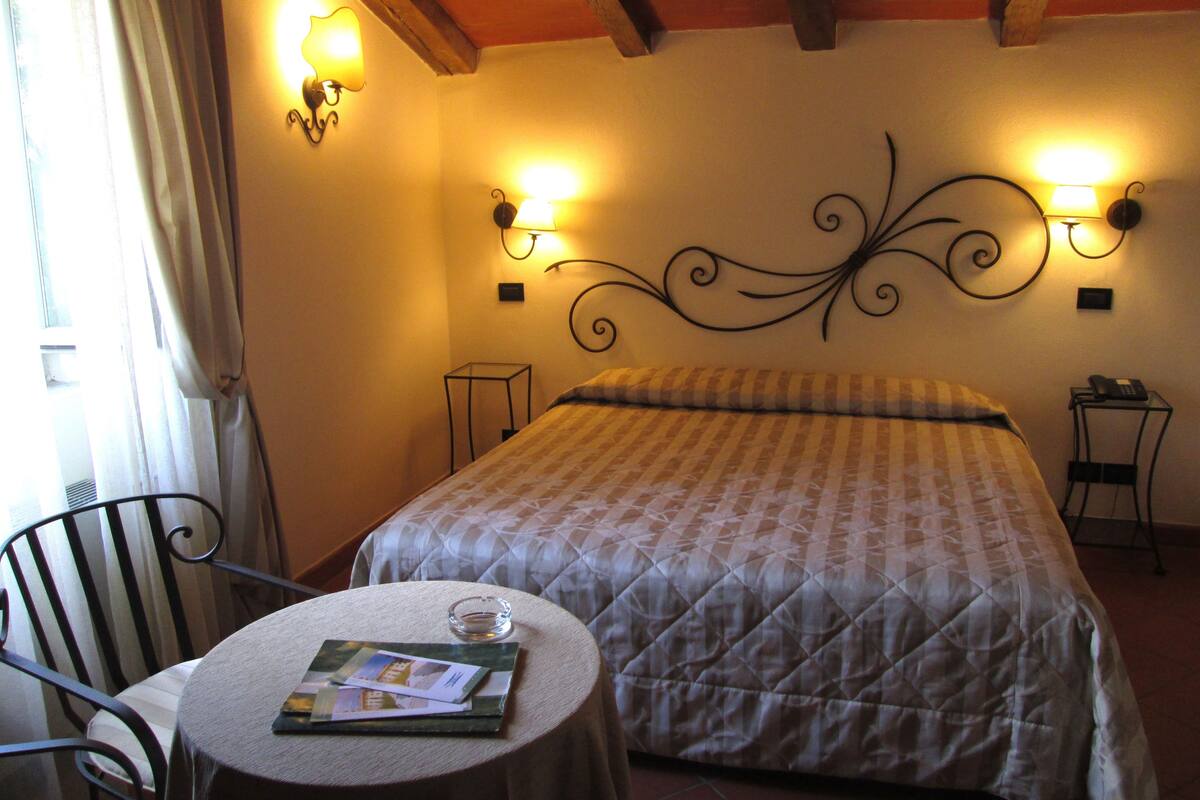 Une chambre d’hôtel avec un lit, une petite table sur laquelle se trouvent un verre et des brochures, deux lampes fixées au mur et une chaise.