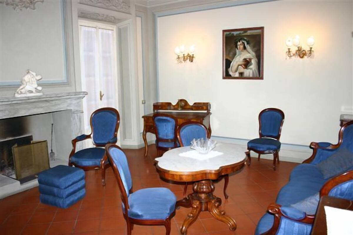A formal dining room with a round table, blue upholstered chairs, and a fireplace.