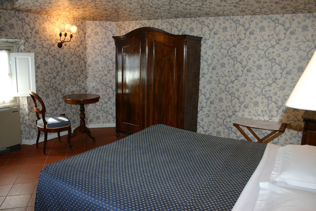 A bedroom with a bed, a wardrobe, a chair, a small table, and a lamp.