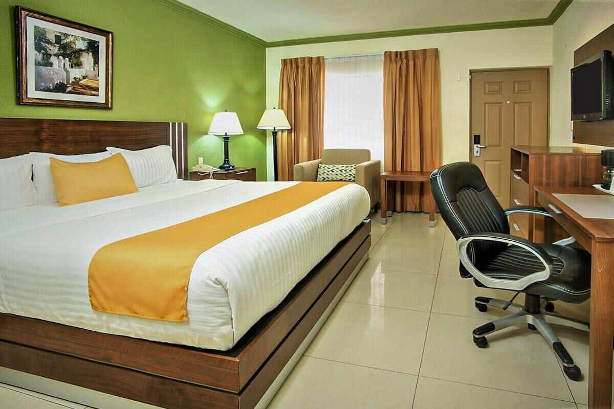 A hotel room with a large bed, a desk, a chair, a television, and a painting on the wall.