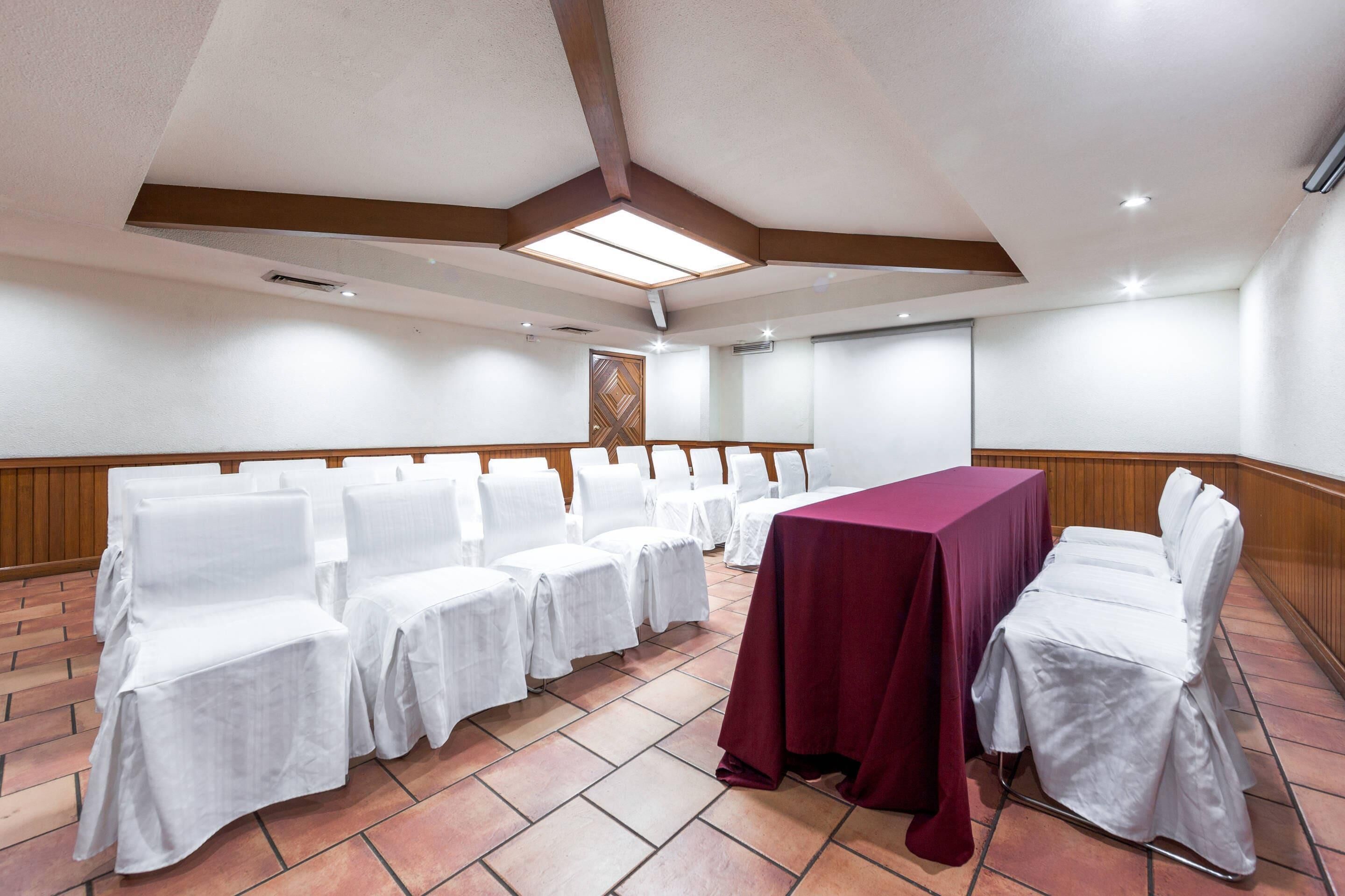 A conference room with white chairs and a table covered with a red tablecloth.