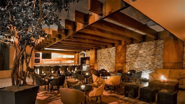 An outdoor seating area with multiple tables and chairs, a stone wall, and a staircase leading to an upper level. - Quality Inn Ciudad Obregon (Cajeme)