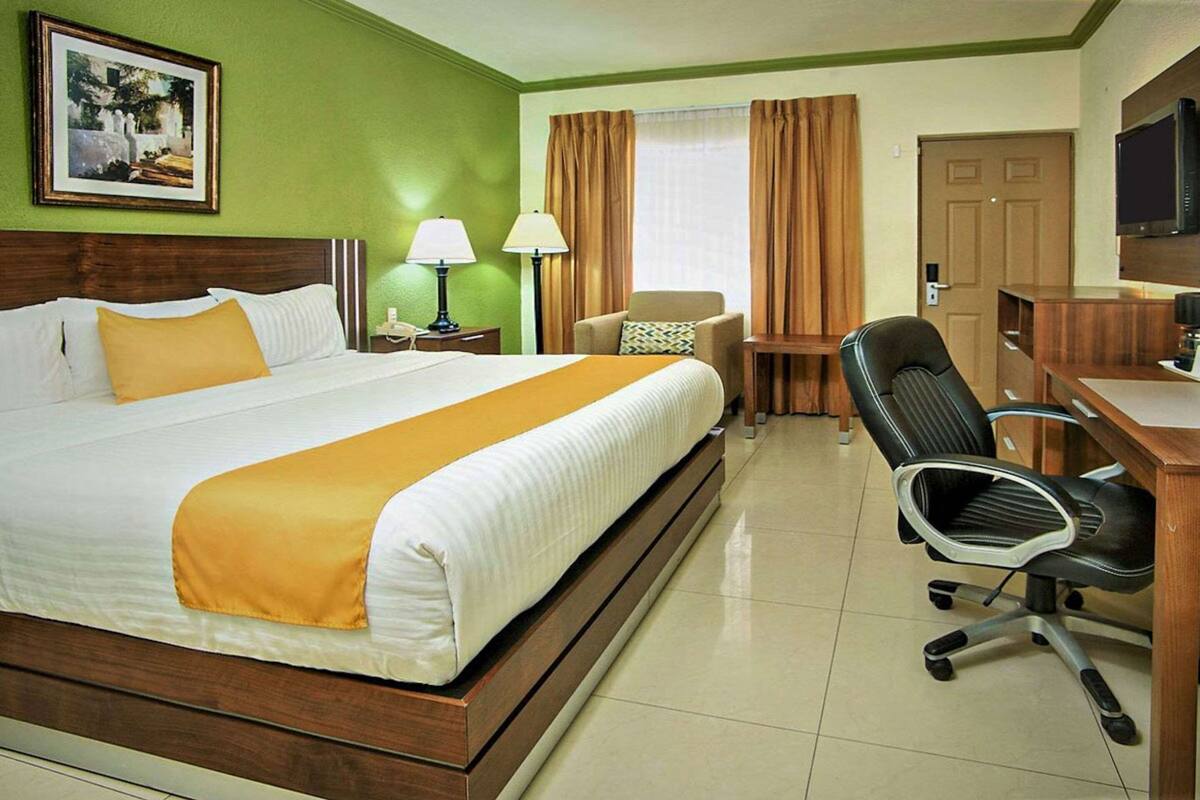 A hotel room with a bed, a desk, a chair, a lamp, a telephone, and a television.
