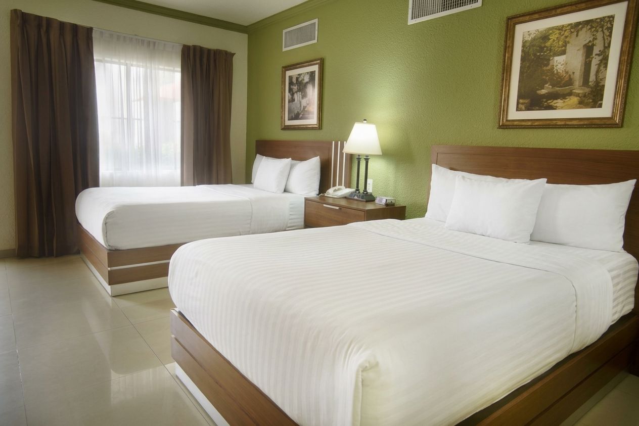 A hotel room with two beds, a nightstand with a lamp, and a painting on the wall.