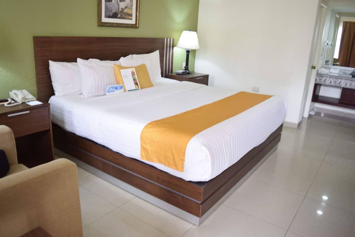 A hotel room with a large bed, a bedside table with a lamp, a chair, and a phone.