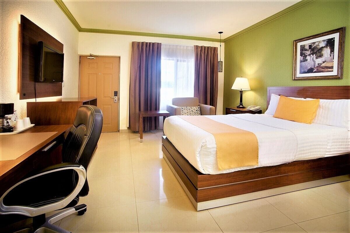 A hotel room with a bed, desk, chair, and a television mounted on the wall.