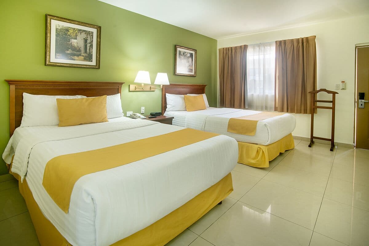 A hotel room with two beds, green walls, and a window with curtains.