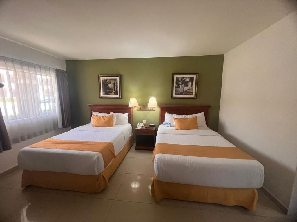 A hotel room with two beds, a nightstand, and two wall-mounted lamps.