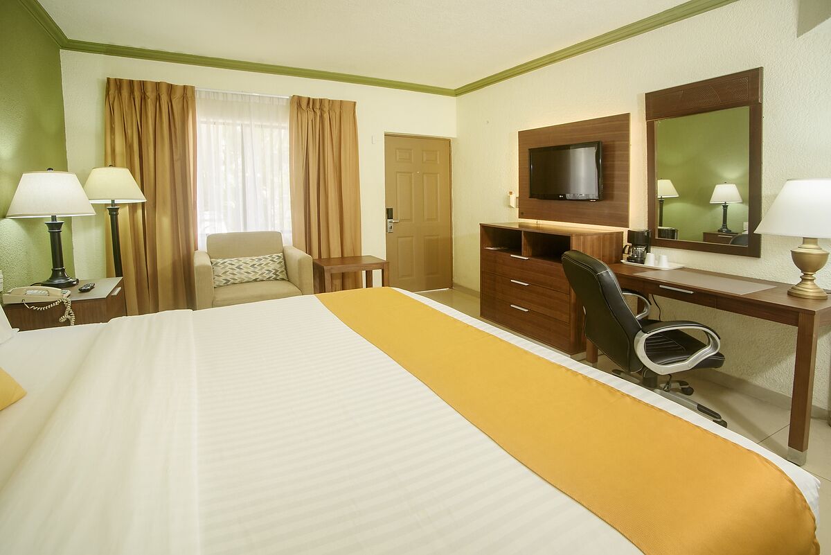 A hotel room with a bed, a desk, a chair, a television, and a mirror.
