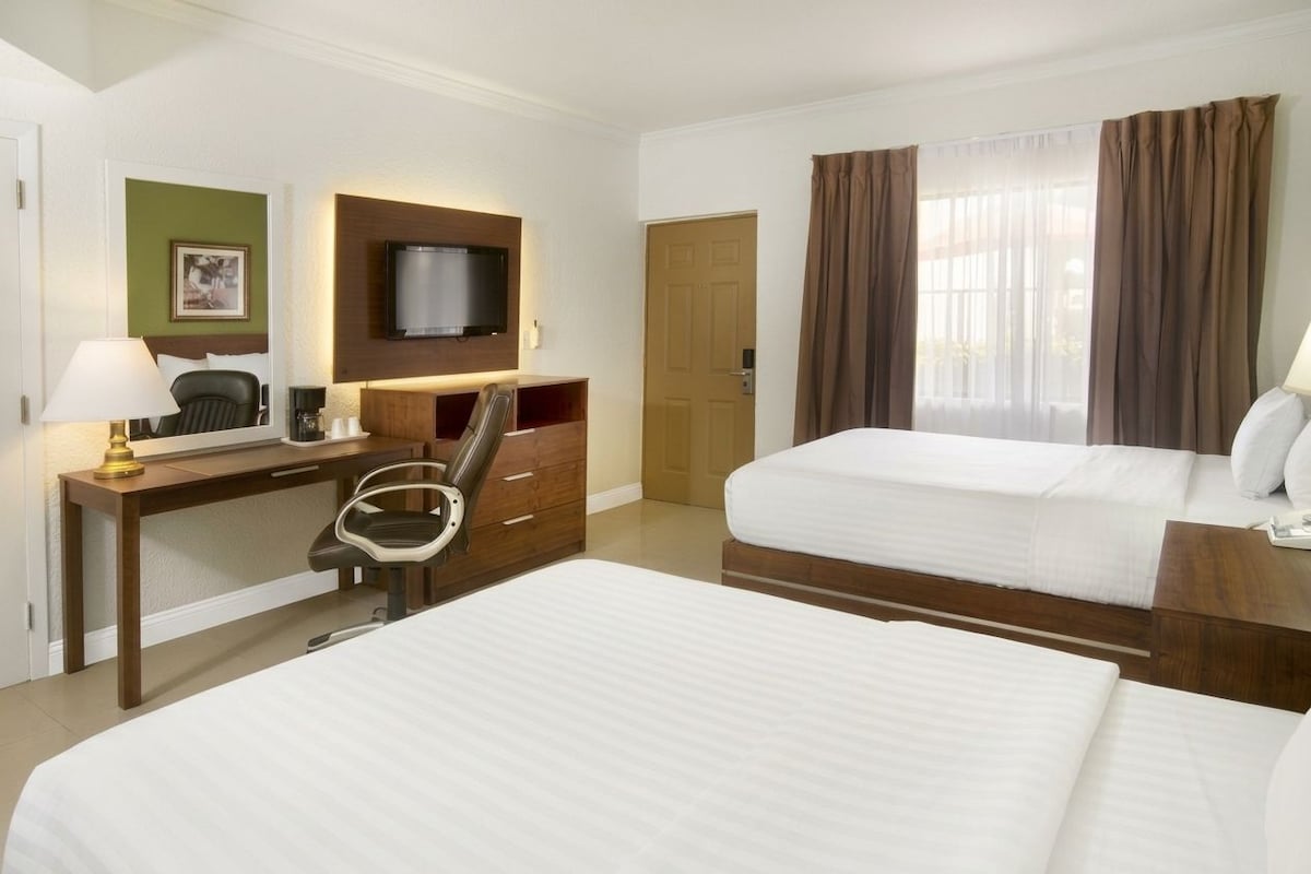 Una habitación de hotel con dos camas, un escritorio con una silla, un televisor y una puerta.