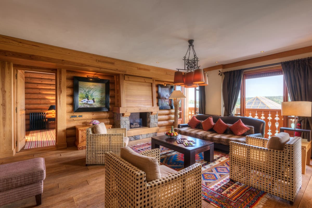 A log cabin interior with a fireplace, wicker furniture, and a view of the outdoors.