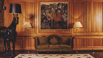 A room with a wooden paneled wall, a green upholstered sofa, two standing lamps, and a horse statue.