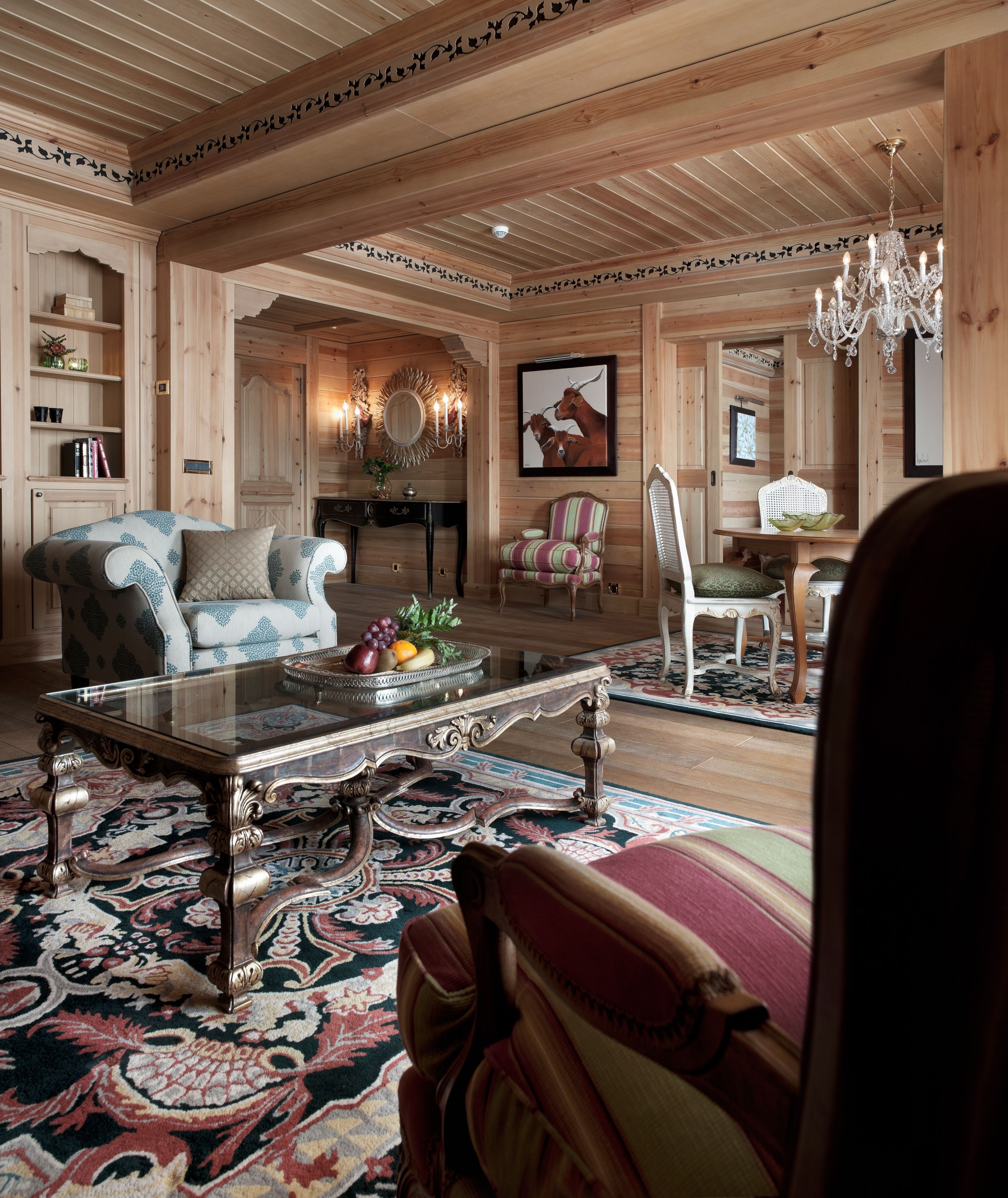 A spacious living room with a large wooden ceiling, a glass coffee table, and a patterned rug.
